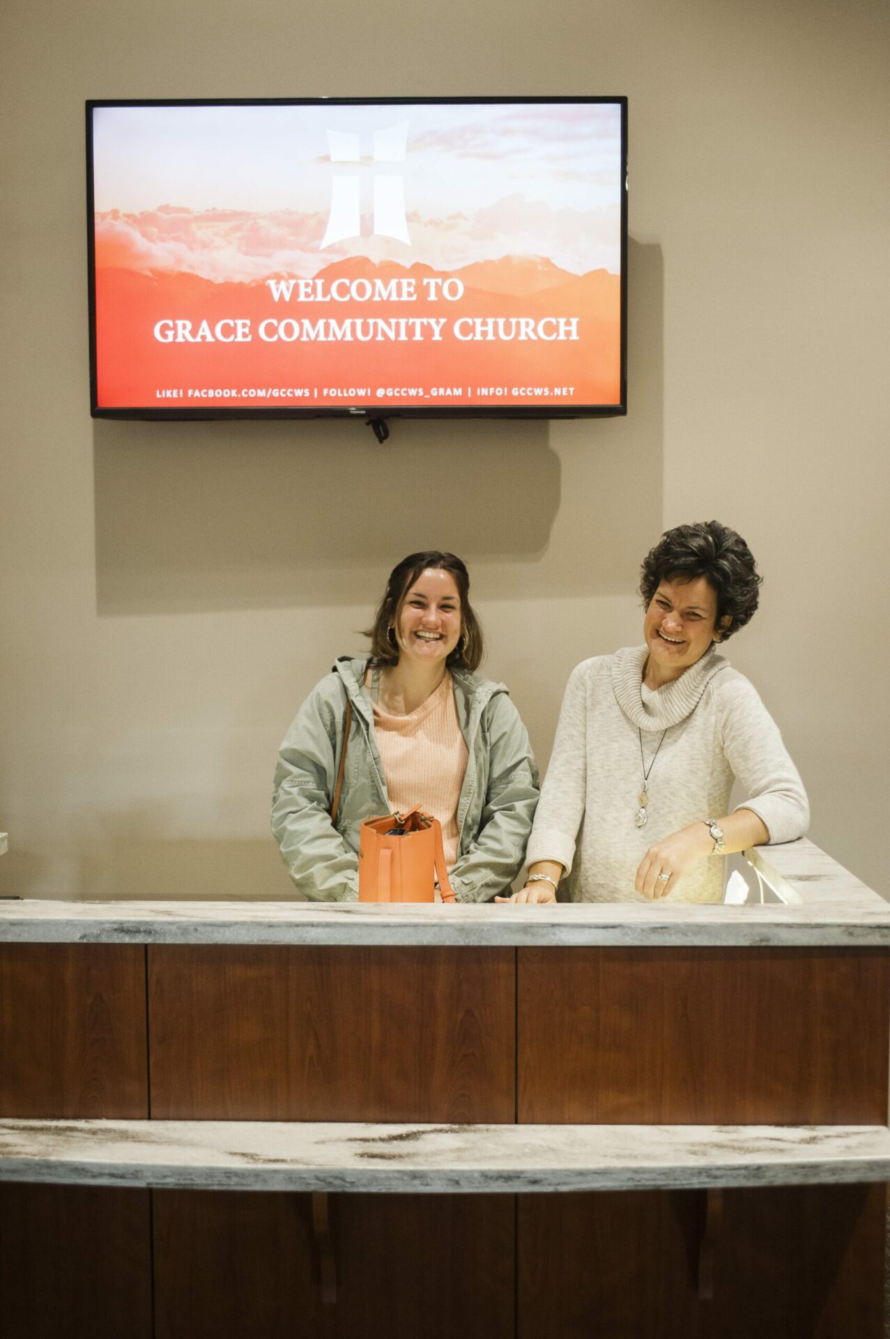 Two Volunteer Women at Welcome Desk Looking at Each Other